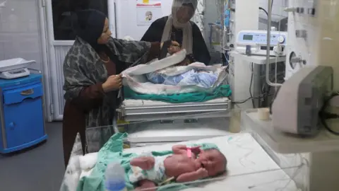 Reuters Mulheres palestinas ao lado de um bebê recebendo tratamento na unidade de cuidados neonatais do Hospital Nasser em Khan Yunis, sul de Gaza (18 de dezembro de 2025).
