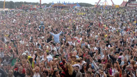 Getty Images Hundreds of people can be seen in a concert crowd with arms aloft.