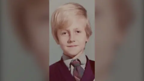 Steve Damon Steve Damon is pictured as a child in the 1970s. The image is a school photograph and Steve is wearing a grey shirt, a dark coloured v-neck jumper and a green and burgundy school tie. He has floppy blonde hair. He looks sad in the picture.