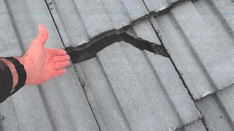 Someone gesturing towards a huge cracked tile on a roof
