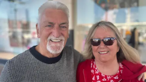 Gary and Janet Taylor smiling at the camera in Cwmbran, and he has his arm around her 