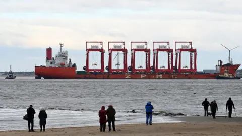 Getty Images The Chinese heavy lift vessel Zhen Hua 36 is seen as it transports a new cantilever rail-mounted gantry, escorted by tug pilot boats, as it enters the River Mersey destined for a deep-water container terminal.