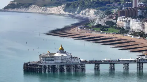 A 19th-century seaside pier in England. Cliffs and a big wheel can be seen on land in the background.