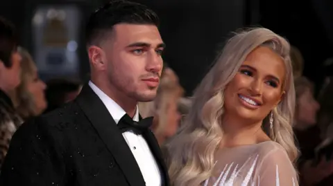 Getty Images Tommy Fury in a black suit and Molly-Mae Hague in a light dress