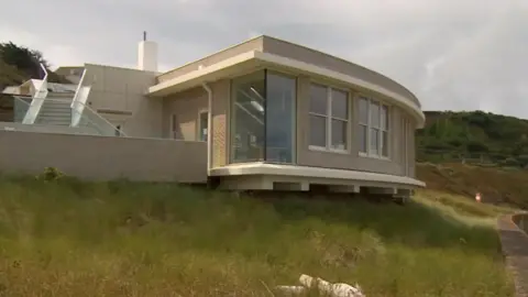 A wide shot of the empty former restaurant building. It is built on the seafront.