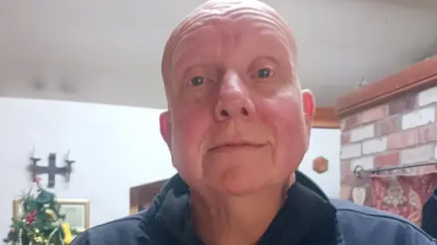 David Platt A bald, clean shaven man is looking at the camera. He is wearing a blue top with a collar, and there is a Christmas tree behind him.