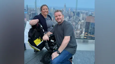 Family handout Allison and David Friday smiling for the camera at the top of a tall building. Allison is in her wheelchair with David kneeling beside.
