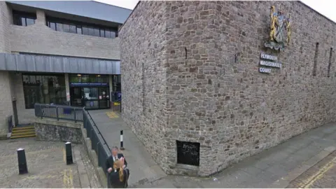 A photo which shows Plymouth Magistrates' Court and Plymouth Youth Court. On the left is a building with windows and double doors. There is a ramp leading up to the doors on the right and stairs on the left. Next to the ramp is a brick building which has Plymouth Magistrates Court on the right of the building with a crest.