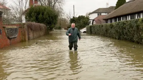 BBC A man wades through floodwaters after the Thames overtopped its banks this winter