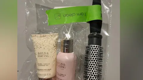 Kerry Galliano A see-through plastic packet containing a round hairbrush and two Baylis & Harding bathroom bottles. A green label says 