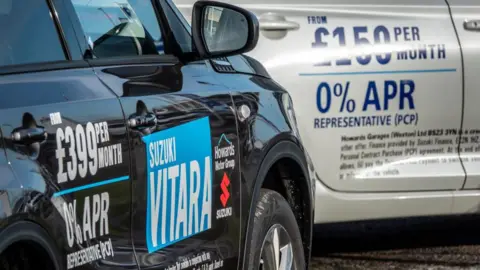 Getty Images Two cars in a dealership with information about financing options written on the cars