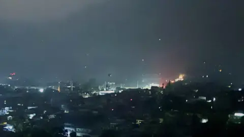 Reuters A picture showing an explosion in the background. It is night, and the lights from homes and street lamps can be made out but it is dark so not much is clear