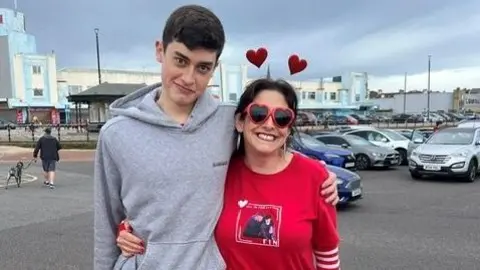 Ellie Wong An older teen in a grey hoodie with a woman in a red jumper and heart deeley boppers 