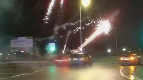 Nightime scene on a major road with cars. Fireworks are coming out of one car,