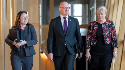 PA Media John Swinney walking up the "glass corridor" at Holyrood with his deputy Kate Forbes and the finance secretary Shona Robison