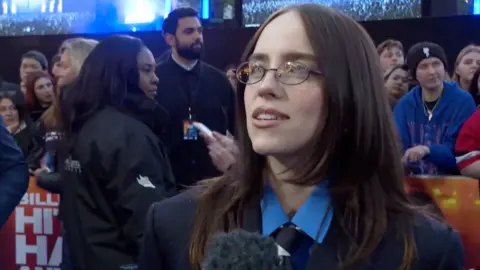 Billie Eilish has shoulder length brown hair and oval glasses on the red carpet