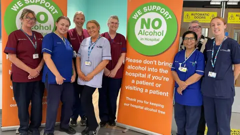 Royal Liverpool University Hospital The University Hospital Liverpool Group’s Alcohol Care Team stand around a poster, smiling, which reads 'We support no alcohol in hospital'. 