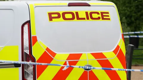 Blue and white police tape and branded police van with red and yellow pattern.