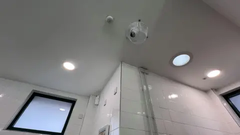 White ceiling of public toilet with CCTV camera behind white wiring 