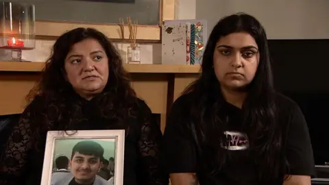 Pooja and Nikita Kanda looking sad at the camera, holding a photo of Ronan