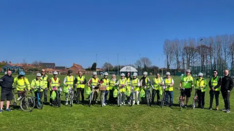 East Riding of Yorkshire Council A group of people holding bikes and wearing hi-vis jackets and helmets standing in a line in a field.