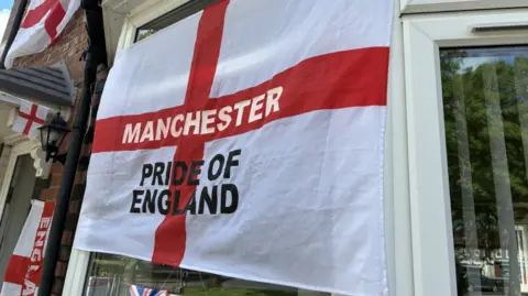 A close up of a St George's flag which has text on it reading 'Manchester PRIDE OF ENGLAND'