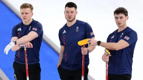Getty Images Three men stand on the ice in blue Team GB shirts with their hands on their Team GB curling brooms
