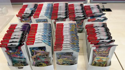 Warwickshire Police Multiple packs of Pokémon trading cards in rows on a table.
