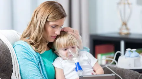 Getty Images A woman holds a child with an oxygen mask on