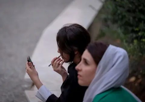 Getty Images Twee vrouwen zitten op een bankje in het park. De een draagt ​​een hoofddoek, de ander niet.