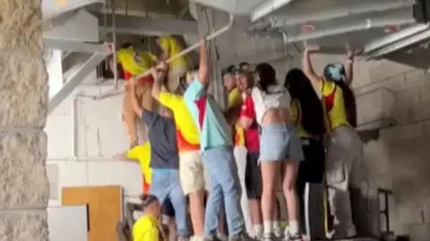 A group of Colombia fans grouped together and standing on a raised platforms climbing into a ventilation shaft.