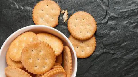 Ritz crackers seen in a bowl with some broken crackers outside of the bowl
