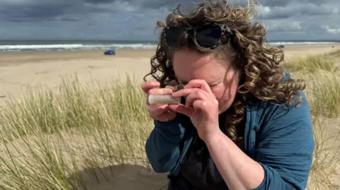 Mel McQuitty looks at a small tube while sitting on Benone Strand on the north coast.