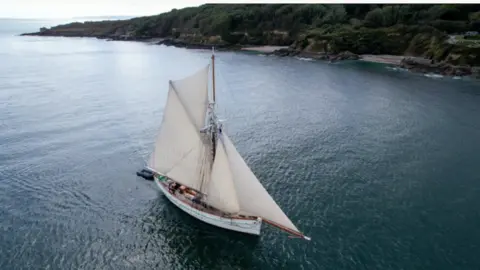 Turn to Starboard An aerial view of The Pellow in full white sails sailing in dark blue sea near the shoreline