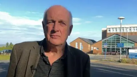 Kevin Earley, wearing a tweed jacket and a shirt, outside Shotley Bridge Hospital.
