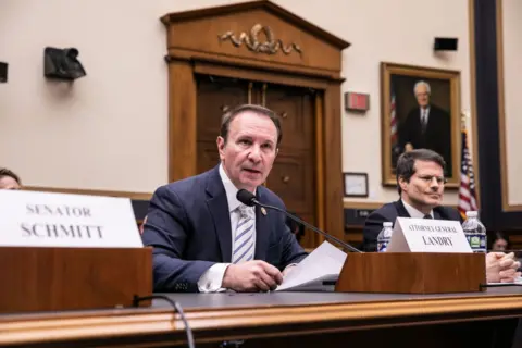 Man holds piece of paper in front of microphone at congressional hearing