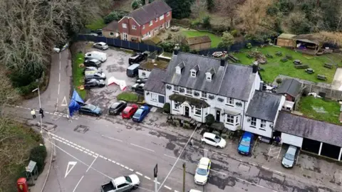 PA Media Aerial view of a large grey pub with a police cordon closing the road outside.