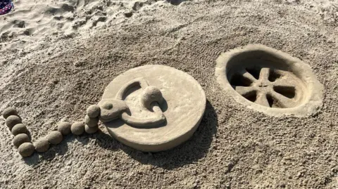 Mark Lewis A giant plug on a chain and a plughole carved out of sand.