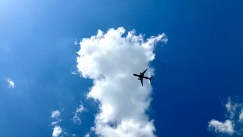 S pace A jet plane with two engines flies in front of a white cloud with a blue sky in the background