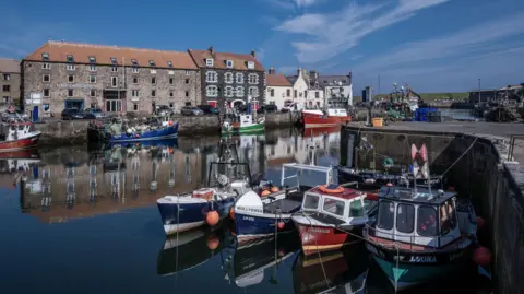 Eyemouth harbour with fishing boats in the foreground, buildings in the background and blue skies overhead