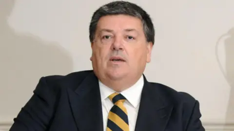 A man wearing a black blazer with a black and yellow tie.