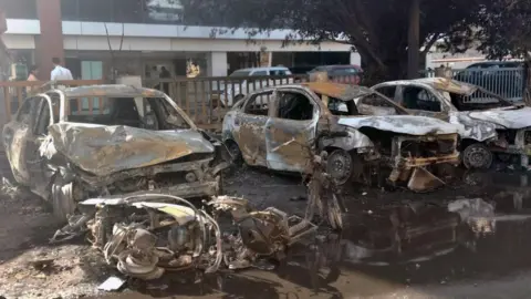Hindustan Times via Getty Images Charred remains of vehicles set ablaze by protestors at a parking are in Sector 63 of Noida on 13 April 2026.