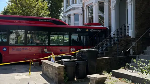 A red bus is crashed into the front of a building. 