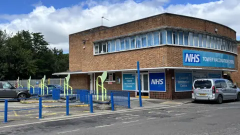 The picture shows the former bus stops and one of the buildings on the site.  It is covered in NHS livery as the site was once a Covid vaccination centre.
