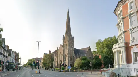 A Google Streetview showing church building with a tall spire at a junction in Leicester.