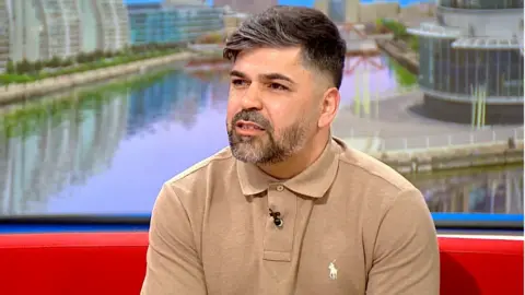 Alice's father Sergio Aguiar, wearing a beige shirt, sits on a red sofa in the BBC Breakfast studio.