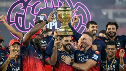 Royal Challengers Bengaluru's Virat Kohli, along with his former team-mates AB de Villiers and Chris Gayle, celebrates with the trophy after winning the Indian Premier League.
