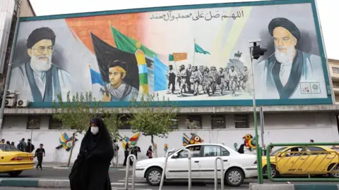 EPA An Iranian female walks past a wall coating of Iranian Supreme Leader Ayatollah Ali Khamenei and erstwhile Iranian Supreme Leader Ayatollah Ruhollah Khomeini successful Tehran (21 October 2024)