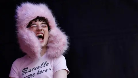 Nemo, wearing a piunk fluffy hat and a t-shirt with the legend 'Marcello come here'
