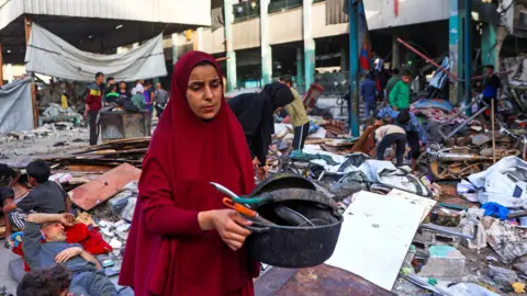 A woman collects salvagable goods with rubble and materials all around her in the middle of the Fahmi Al-Jargawi School courtyard on Monday